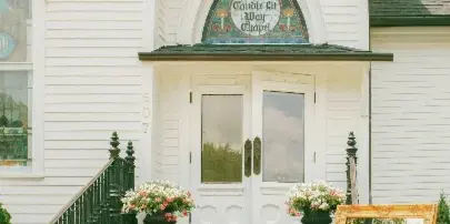 Exterior view of a white Victorian-style event venue with stone steps, floral arrangements, and a wedding welcome sign.