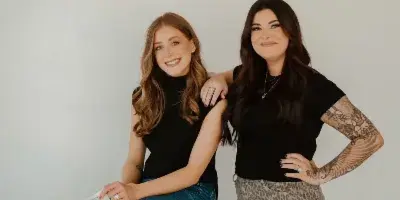 Two women posing together, one holding a newspaper that says 'YOU LOOK SO GOOD'