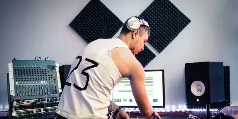 DJ wearing headphones mixing music in a studio with sound equipment.