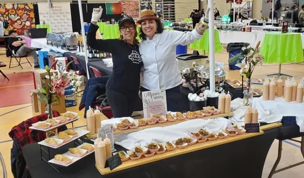 Two women standing behind a catering table filled with appetizers and food displays, with a sign reading 'Alfonso's Catering'.