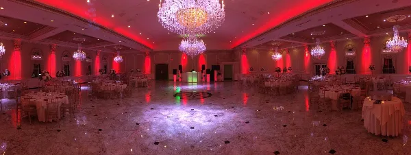 A wedding reception hall with a dance floor, DJ booth, and red ambient up-lighting.