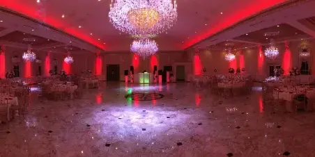 A wedding reception hall with a dance floor, DJ booth, and red ambient up-lighting.