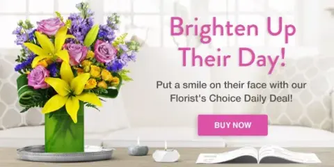 A colorful floral arrangement featuring yellow lilies and pink roses in a green vase, displayed on a table in a bright room.