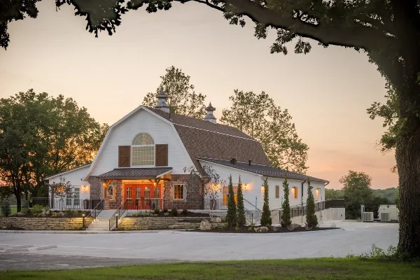 Exterior view of a white and stone wedding venue building with a red door at dusk.