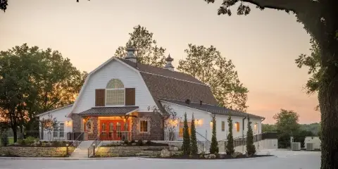Exterior view of a white and stone wedding venue building with a red door at dusk.