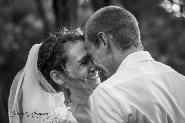 Black and white photo of a bride and groom touching foreheads and smiling.