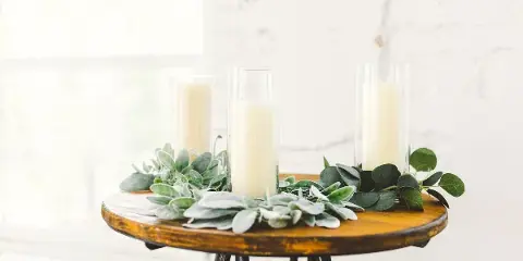A rustic wooden table stand decorated with greenery and tall candles in glass holders, representing wedding decor styling.