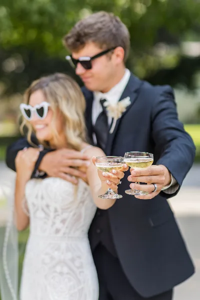 A bride and groom in formal wedding attire toasting with champagne glasses outdoors.