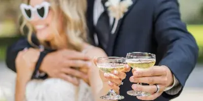A bride and groom in formal wedding attire toasting with champagne glasses outdoors.