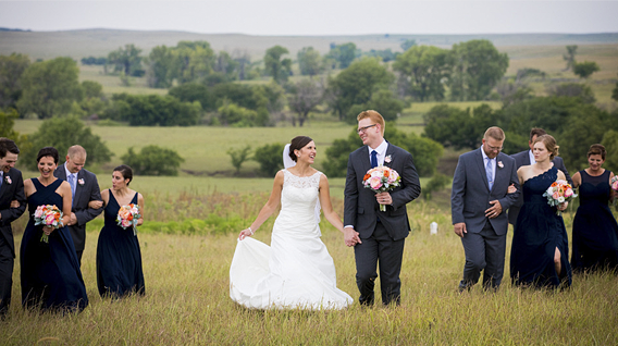 A bride and groom walking down a grassy aisle with their wedding party in a rural field setting.