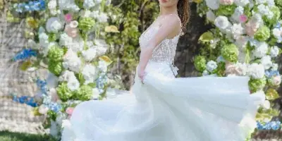 A bride in a white wedding dress standing outdoors in front of a floral arch, showcasing her bridal hair and makeup.