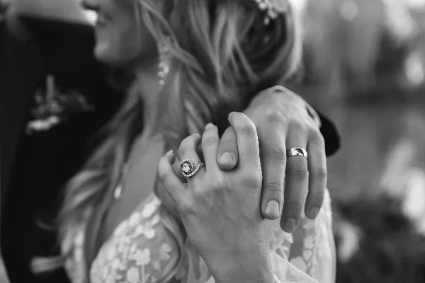 A black and white close-up of a bride and groom's hands intertwined, showcasing their wedding rings.