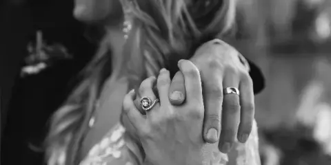 A black and white close-up of a bride and groom's hands intertwined, showcasing their wedding rings.