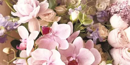 A close-up of a floral arrangement containing pink orchids, roses, and delphiniums wrapped in paper.