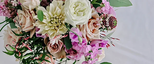 A close-up of a lush floral arrangement featuring white and blush roses, a large cream dahlia, and pink lisianthus.