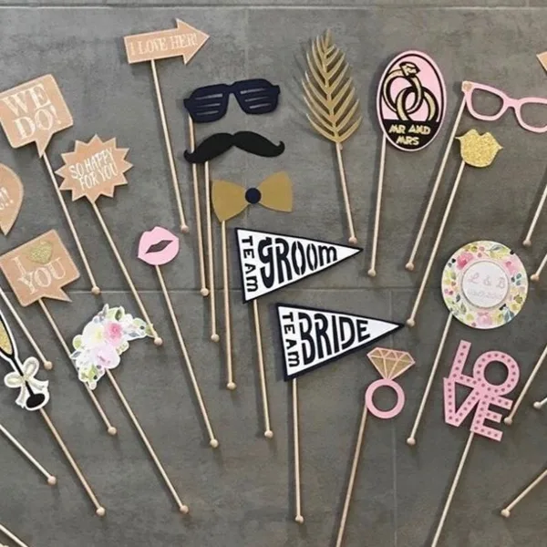 An assortment of wedding-themed photo booth props including flags, glasses, and mustaches arranged on a grey surface.