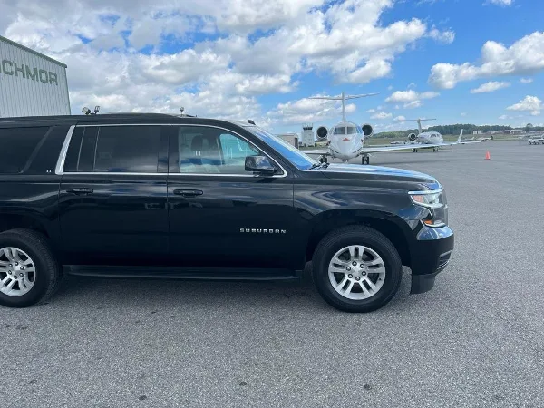Black Chevrolet Suburban SUV parked on an airport tarmac with a private jet in the background.