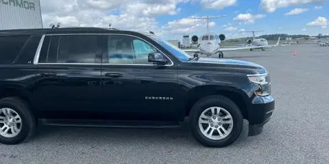 Black Chevrolet Suburban SUV parked on an airport tarmac with a private jet in the background.