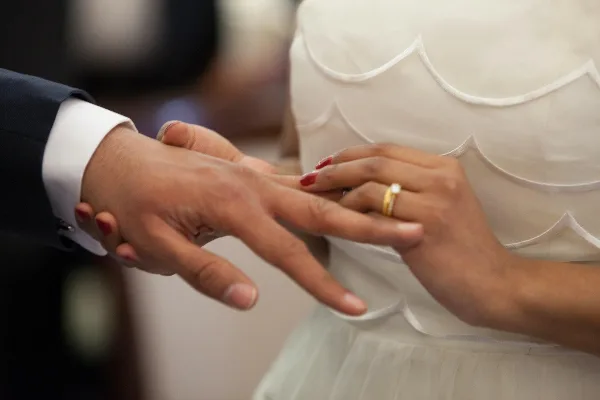 Close-up of a groom placing a wedding ring on a bride's finger during a ceremony.
