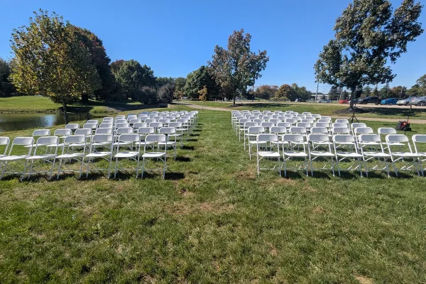 Rows of white folding chairs arranged on a grassy lawn for an outdoor event.