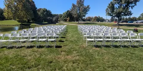 Rows of white folding chairs arranged on a grassy lawn for an outdoor event.