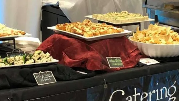 A catering buffet table displaying various gourmet appetizers, including olive feta and potato artichoke bites, with a 'Catering' banner.