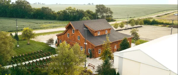 Aerial view of a rustic wooden timber frame barn event center surrounded by green fields and trees.