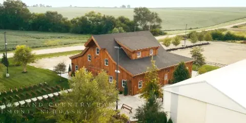 Aerial view of a rustic wooden timber frame barn event center surrounded by green fields and trees.