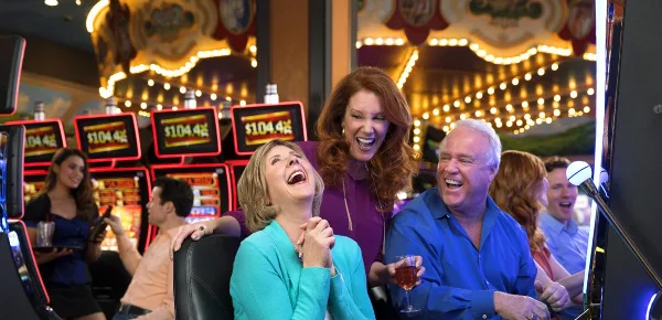 Three people laughing and drinking at a casino.