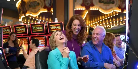 Three people laughing and drinking at a casino.