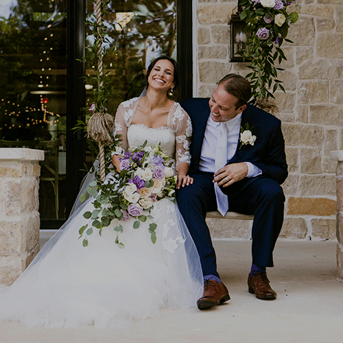 A bride and groom sitting on a stone porch decorated with flowers.