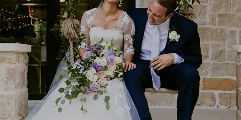 A bride and groom sitting on a stone porch decorated with flowers.
