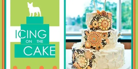 A three-tiered white wedding cake decorated with orange and black floral patterns and topped with a 'We Do' bird topper.
