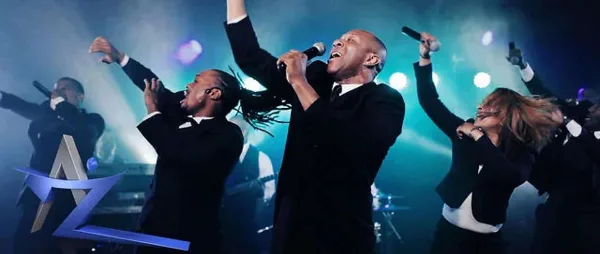 A live vocal band performing on stage with microphones and stage lighting.