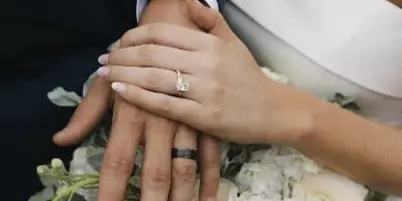 Close-up of a bride and groom's hands holding a white wedding bouquet with hydrangeas and eucalyptus.
