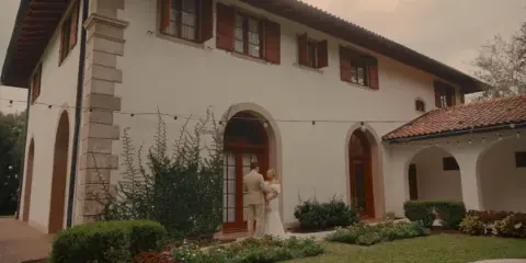Bride and groom standing and reading their wedding vows in front of a white stucco venue building.