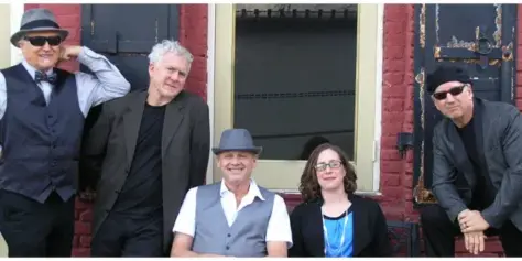 Group photo of the Shaky Ground Band members standing and sitting in front of a red brick building.