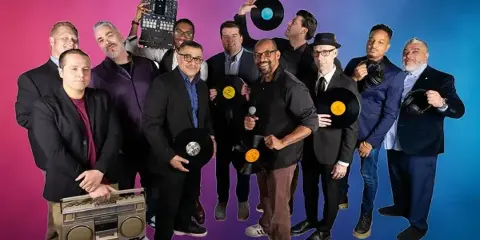A group of professional DJs and event staff posing with turntables, mixers, and microphones.