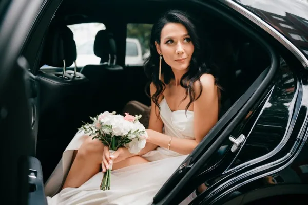 Bride in a white dress holding a bouquet seated in the back of a luxury car