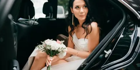 Bride in a white dress holding a bouquet seated in the back of a luxury car