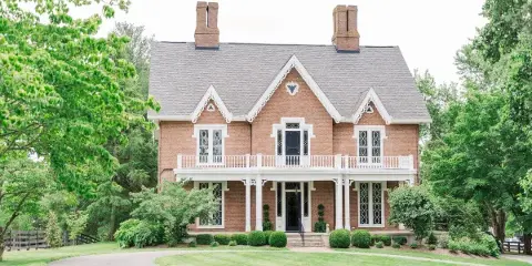 Exterior view of the historic brick Warrenwood Manor house with a white porch and manicured lawn.