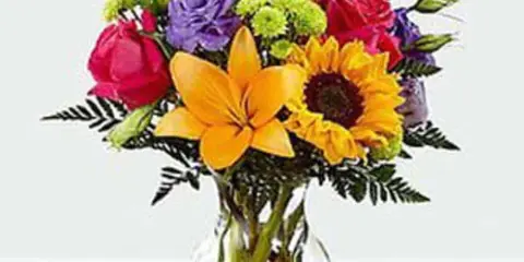 A colorful floral arrangement with sunflowers, orange lilies, and red roses in a clear glass vase.