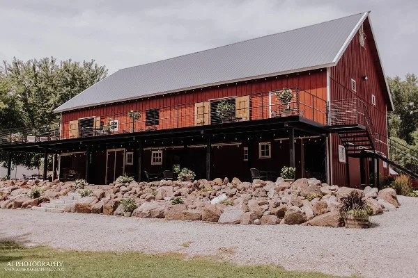 Exterior view of a red barn wedding venue with a metal roof, outdoor deck, and rock landscaping.