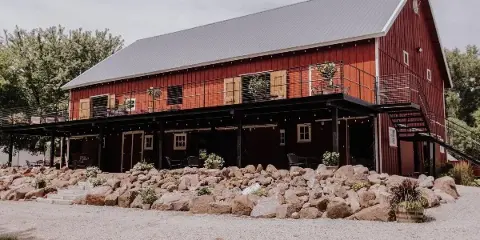 Exterior view of a red barn wedding venue with a metal roof, outdoor deck, and rock landscaping.