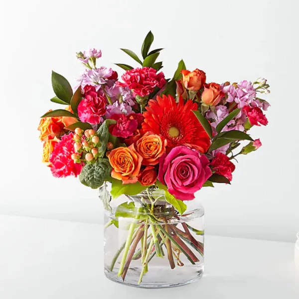 A colorful mixed bouquet of roses, gerbera daisies, and carnations arranged in a clear glass vase.