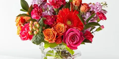 A colorful mixed bouquet of roses, gerbera daisies, and carnations arranged in a clear glass vase.