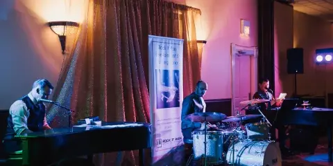 Musicians performing live on stage with pianos and drums in front of a Rock It Man Entertainment banner