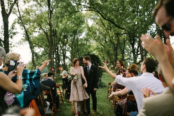 A bride and groom walking down an outdoor aisle as guests throw flower petals.