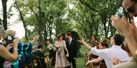 A bride and groom walking down an outdoor aisle as guests throw flower petals.