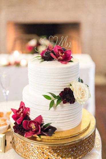 A white two-tier wedding cake decorated with pink and white flowers and a Mr & Mrs topper.